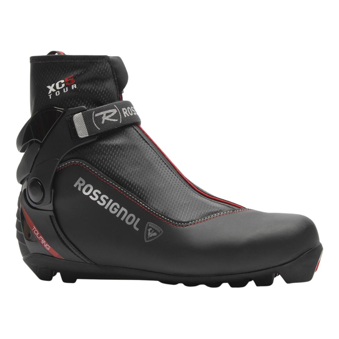 La BOTTE DE SKI DE FOND ROSSIGNOL XC 5 est une chaussure de ski de fond noire avec des accents rouges, une marque grise, une sangle de cheville, un revers de cheville haut, une surface texturée et une semelle robuste conçue pour la randonnée.