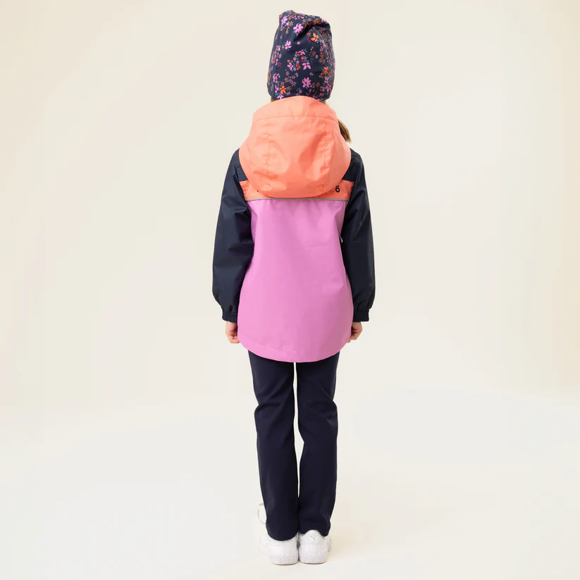 Enfant portant une veste à capuche rose et orange à manches foncées, un pantalon bleu marine, des baskets blanches et un chapeau à fleurs. Il se tient dos à l'objectif sur un fond clair et uni.