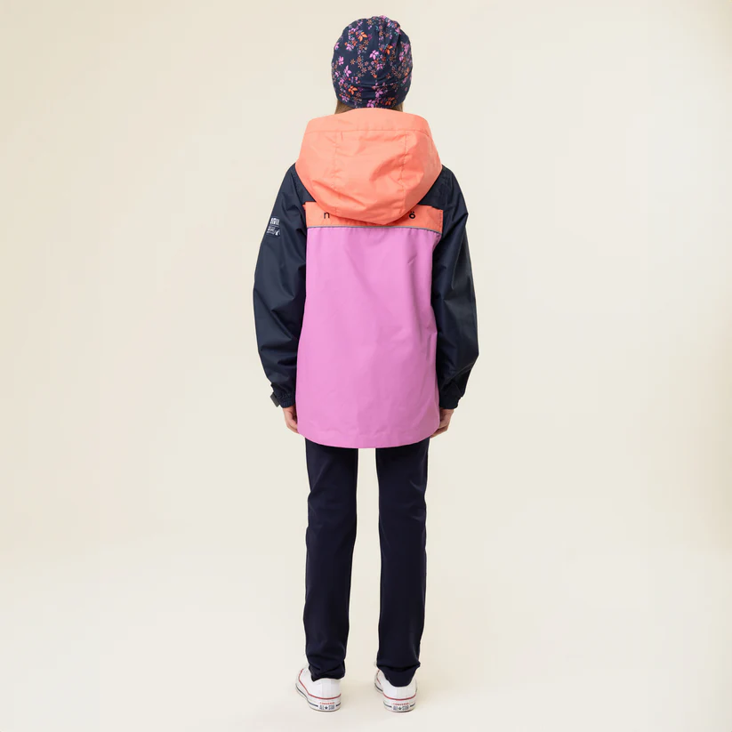 Une personne, tournée vers l'extérieur, porte une veste à capuche rose et orange, un pantalon foncé et un bonnet à motifs floraux. Elle porte des chaussures blanches à semelle marron visible, sur un fond uni et clair.