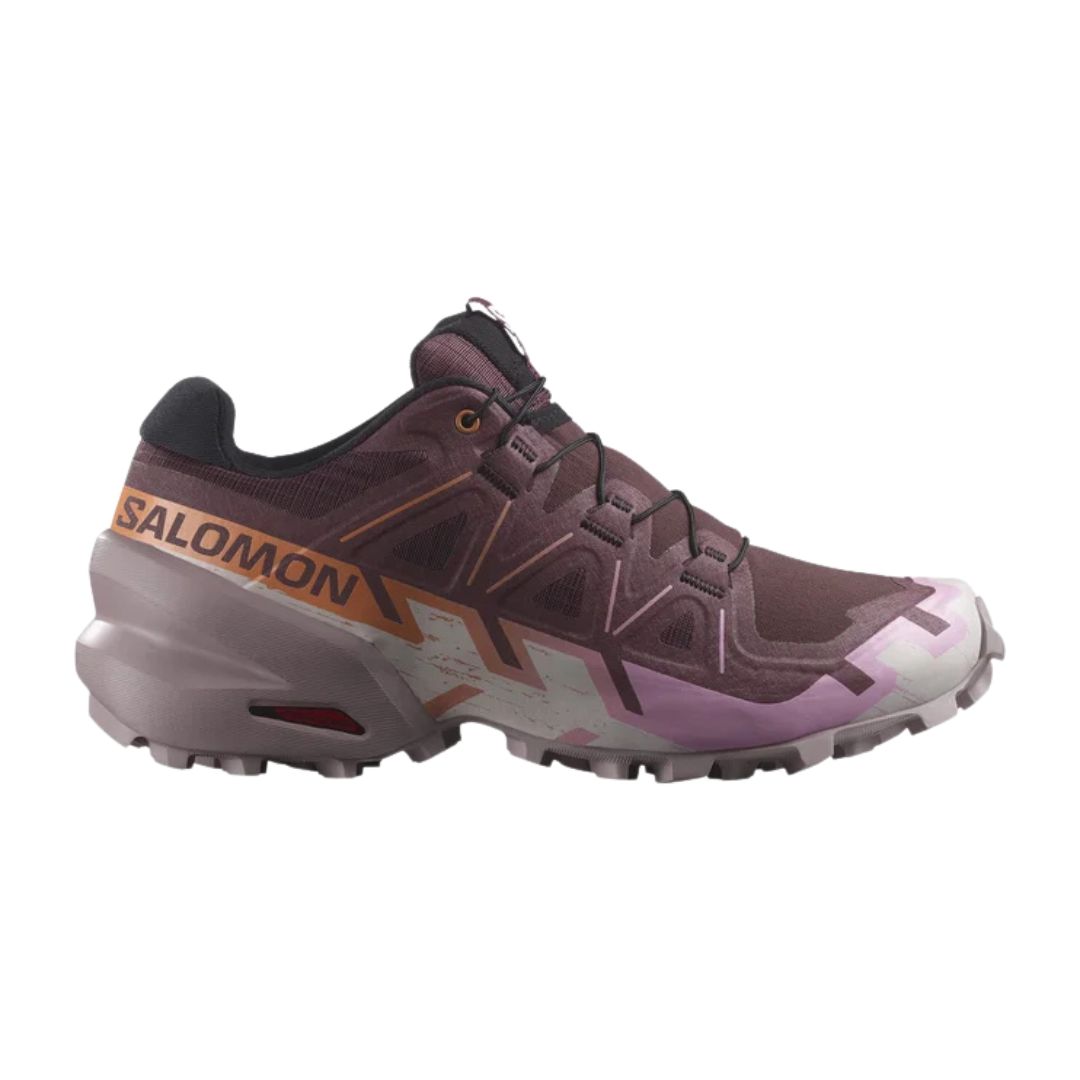 Chaussure unique de trail running, à dominante marron avec des accents roses, blancs et orange, portant le nom de la marque "Salomon" en orange sur le talon et une semelle extérieure rugueuse et texturée pour l'adhérence.