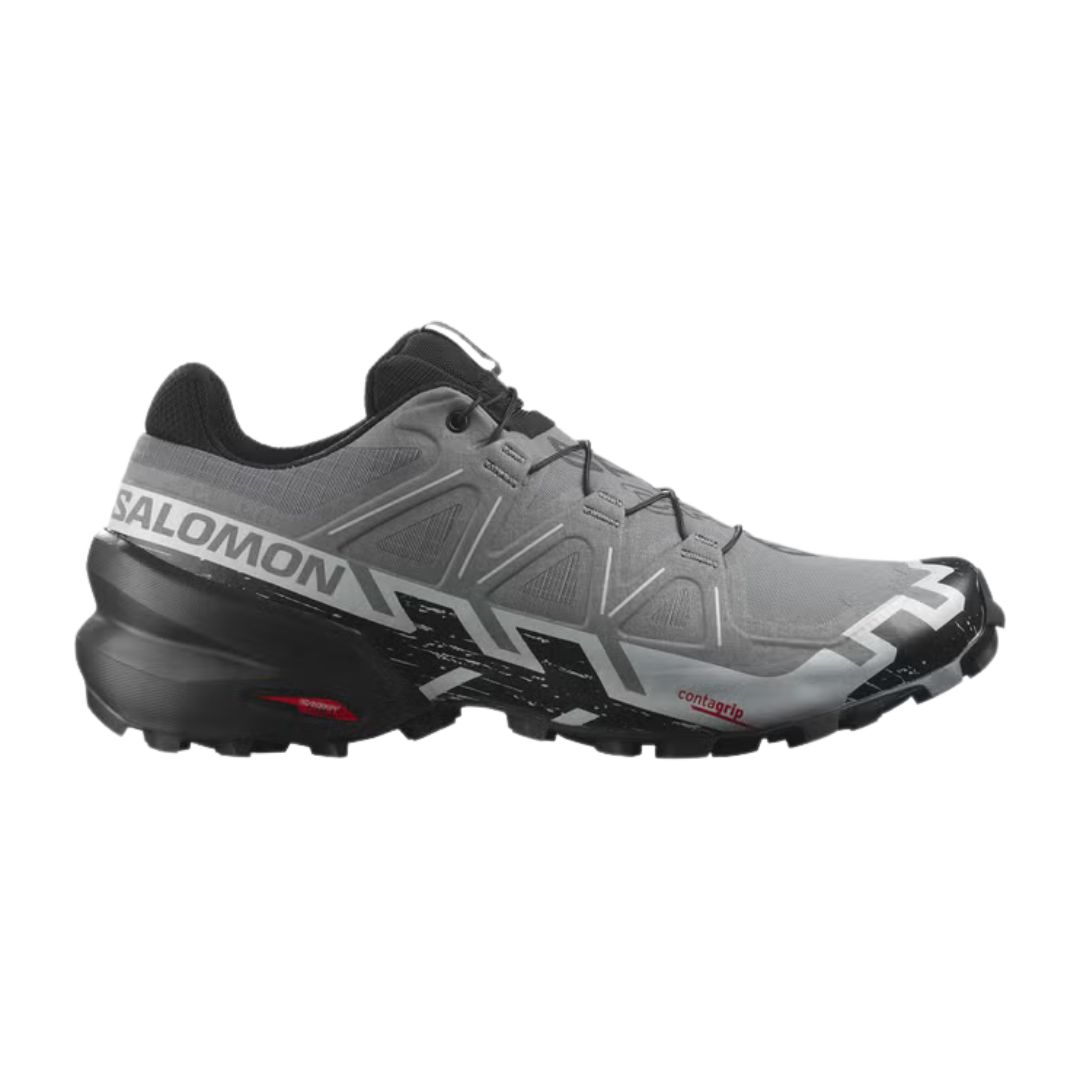 La Salomon SPEEDCROSS 6 WIDE, montrée de profil, présente un design gris et noir avec des bandes de roulement robustes, un marquage latéral blanc et des accents de semelle rouges sur un fond blanc.
