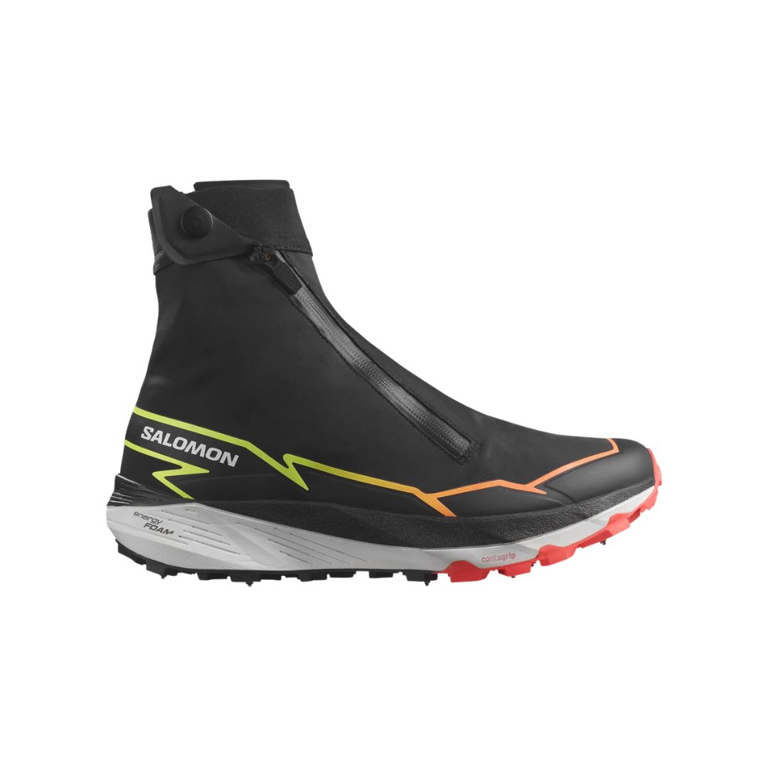 Vue latérale d'une chaussure de sport Salomon noire avec une tige mi-haute zippée. La chaussure présente un design en zigzag jaune fluo vif et une semelle teintée orange avec des adhérences texturées, conçue pour les terrains accidentés et les activités de plein air.