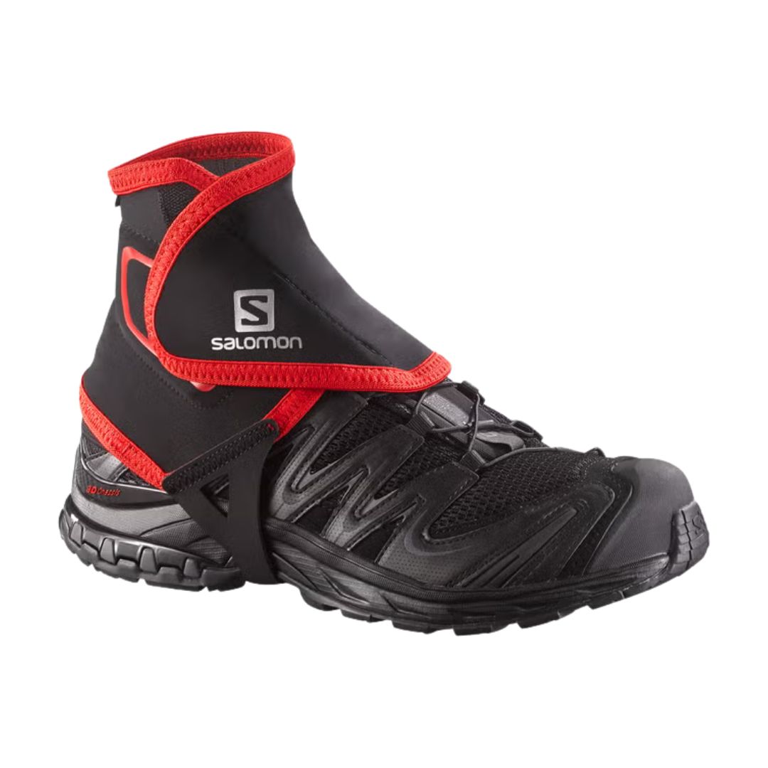 La chaussure de trail Salomon TRAIL GAITERS HIGH noire présente une guêtre de cheville rouge et noire conçue pour empêcher les débris de pénétrer dans la chaussure, sur fond blanc.