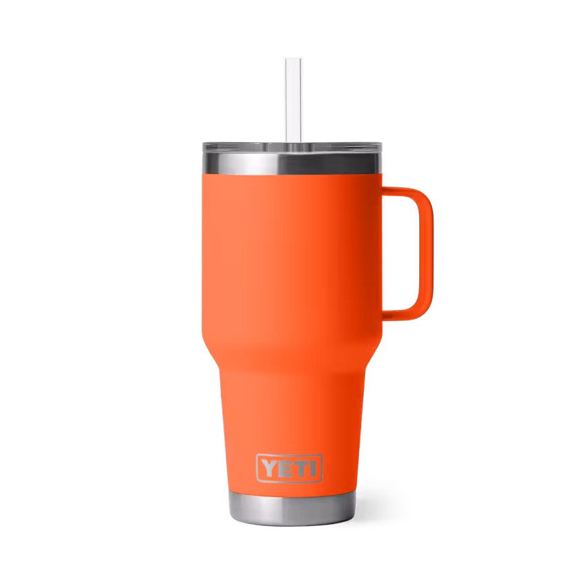 Une tasse de voyage YETI orange vif avec une poignée, un couvercle transparent et une paille transparente, sur un fond blanc uni.