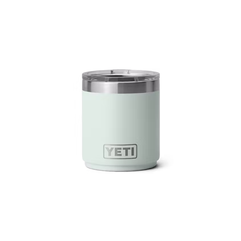 Le RAMBLER 10 OZ LOWBALL 2.0 est un gobelet en acier inoxydable vert menthe clair avec une finition lisse et mate, un couvercle transparent et le logo YETI sur le devant. Le gobelet a un design cylindrique.