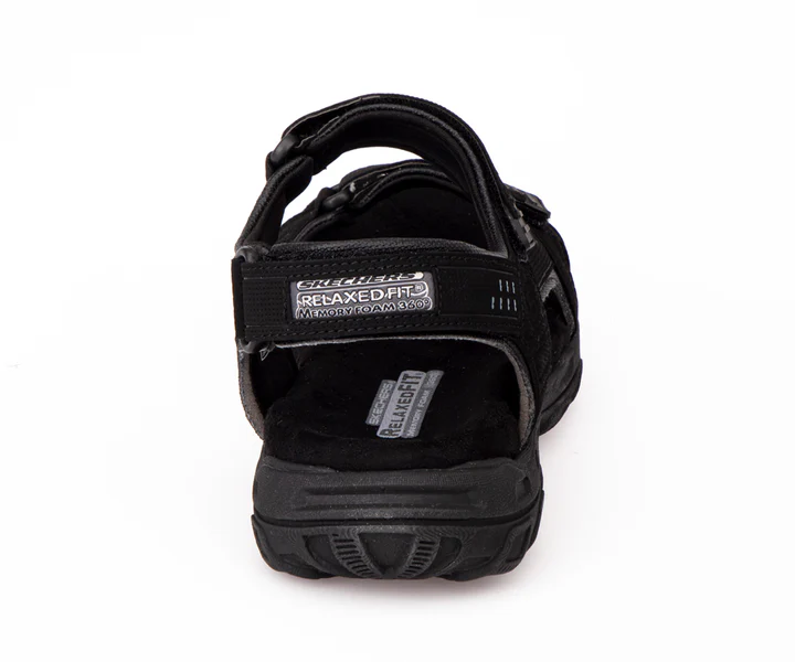Vue arrière d'une sandale noire à bout ouvert avec une semelle épaisse, dotée de sangles réglables et d'une marque visible, y compris les étiquettes « RELAXED FIT » et « SKECHERS ».