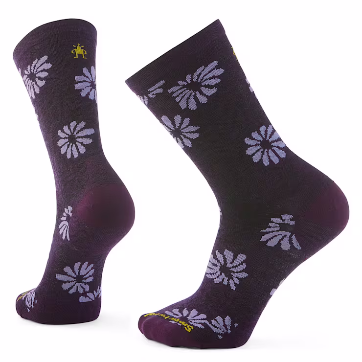 Une paire de chaussettes violet foncé avec des motifs floraux violet clair, présentées sous différents angles. Elles arborent un petit logo jaune près du bord côtelé et un texte jaune sur le bout.