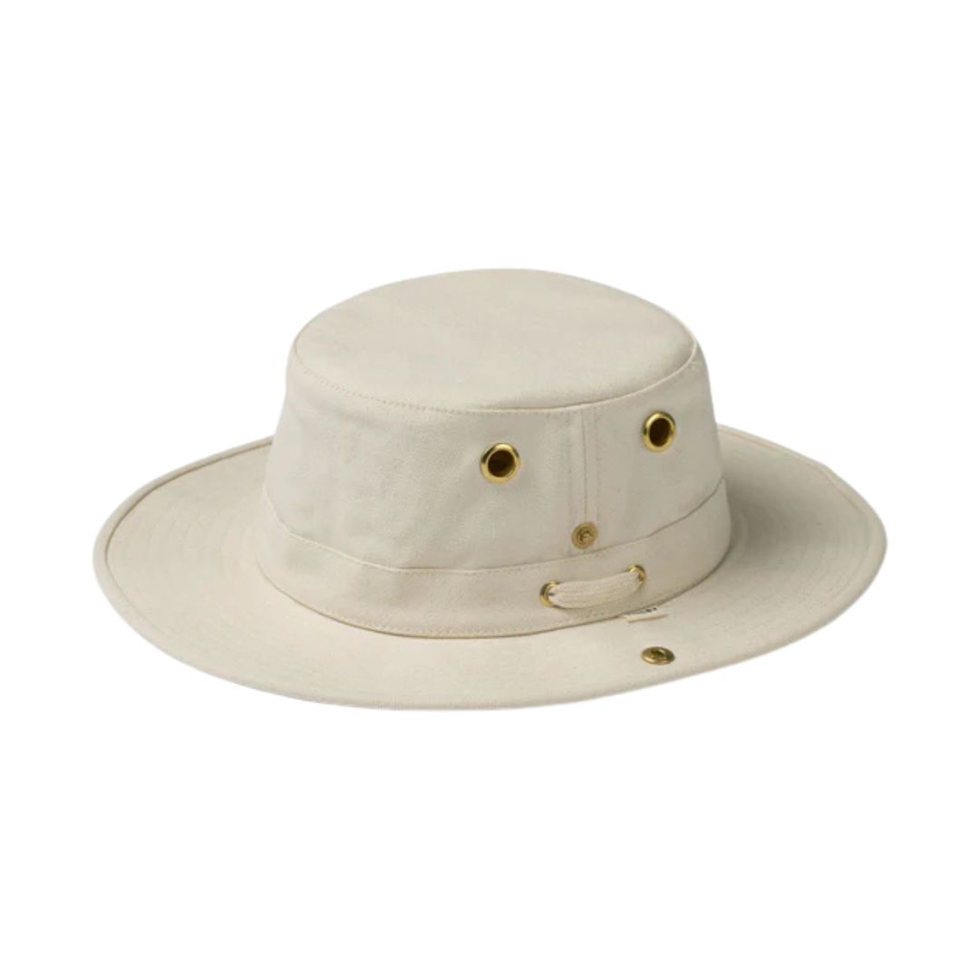Le CHAPEAU TILLEY T3 CLASSIC est un chapeau baquet beige à large bord, doté d'œillets métalliques et d'une petite boucle latérale, disposés de manière à ressembler à un visage souriant.