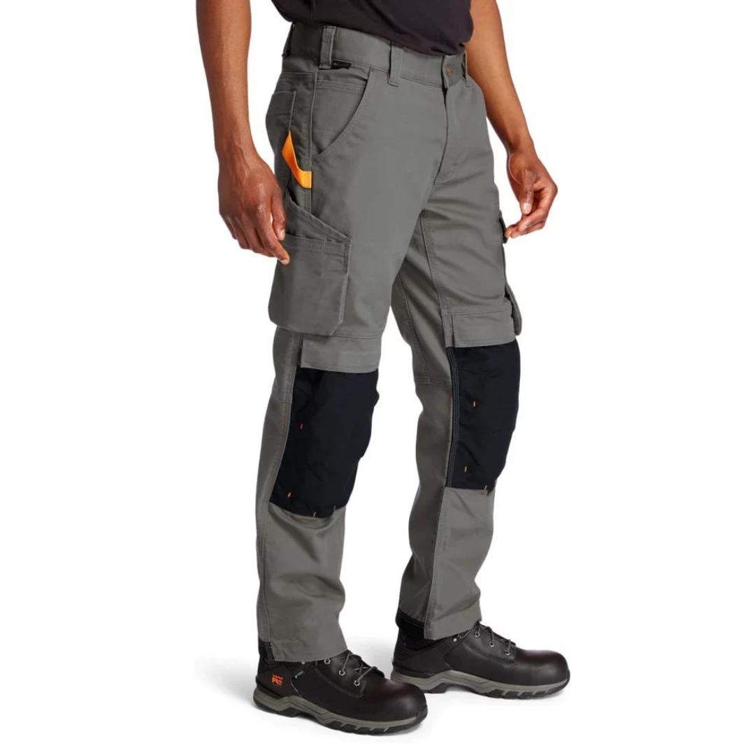 PANTALON DE TRAVAIL TIMBERLAND PRO IRONHIDE FLEX À GENOULLIÈRES POUR HOMME couleur gunmetal porté par un homme vu de la taille aux pieds pantlaon gris acier avec renforts noirs pour les genoullières passants pour la ceinture et ganse pour marteau orangée visible