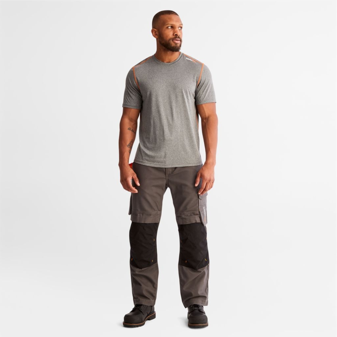 PANTALON DE TRAVAIL TIMBERLAND PRO IRONHIDE FLEX À GENOULLIÈRES POUR HOMME couleur gunmetal porté par un homme vu de face de la tête aux pieds avec le pantalon gris acier renforcé avec un tissu noir aux genoux et poches cargo visibles