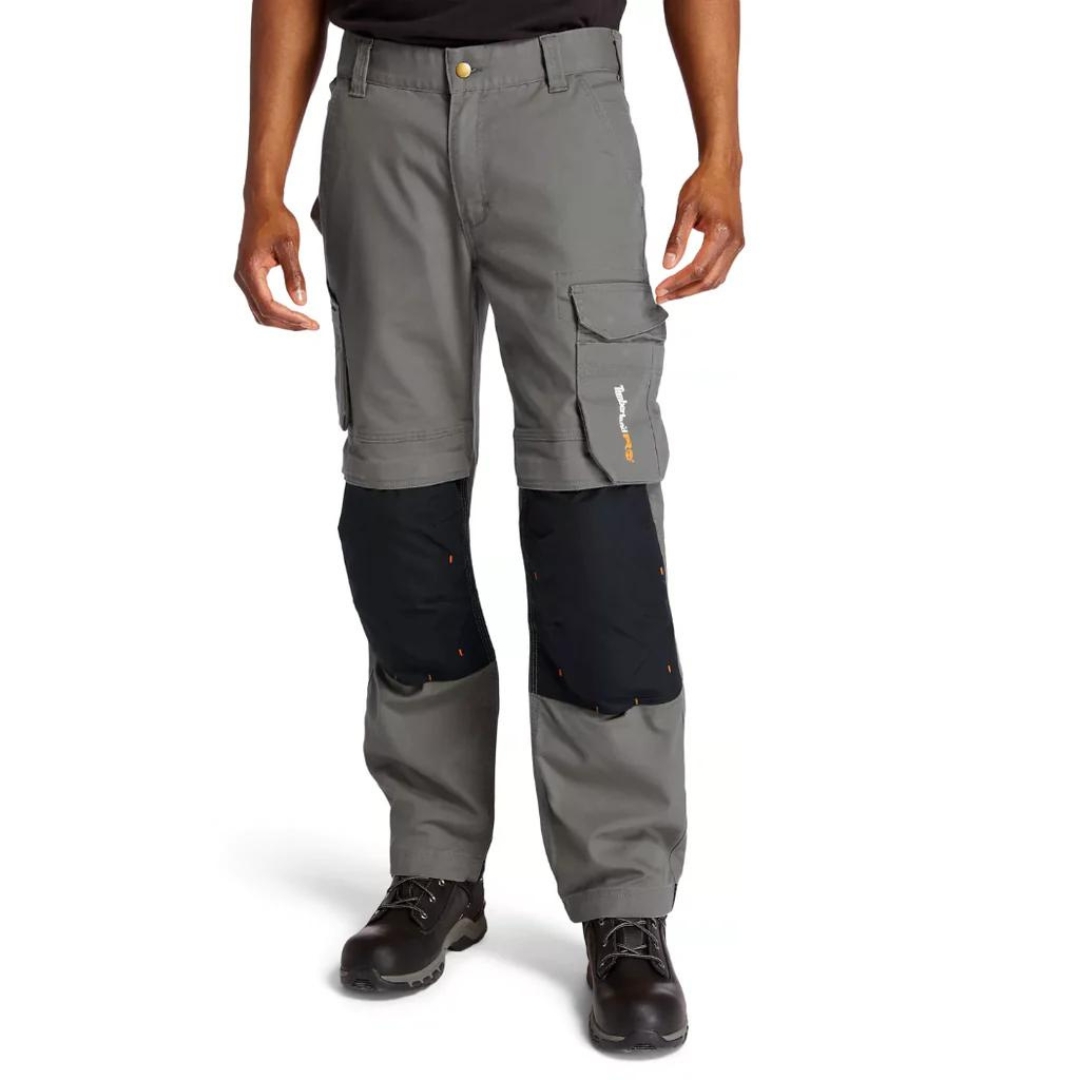 PANTALON DE TRAVAIL TIMBERLAND PRO IRONHIDE FLEX À GENOULLIÈRES POUR HOMME couleur gunmetal porté par un homme vu de face de la taille aux pieds passants à ceinture visible, poche cargo avec le logo timberland pro imprimé visible, renfort en tissu résistant noir aux genoux et pantalon gris acier