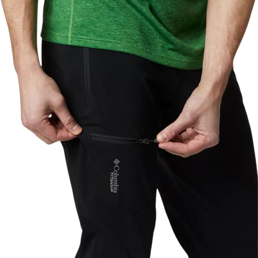PANTALON DE PLEIN AIR COLUMBIA TITAN PASS POUR HOMME couleur black porté par un homme vu en gros plan su rle haut du pantalon il ouvre la fermeture éclair de la poche de cuisse Logo columbia titanium visible sur la cuisse droite