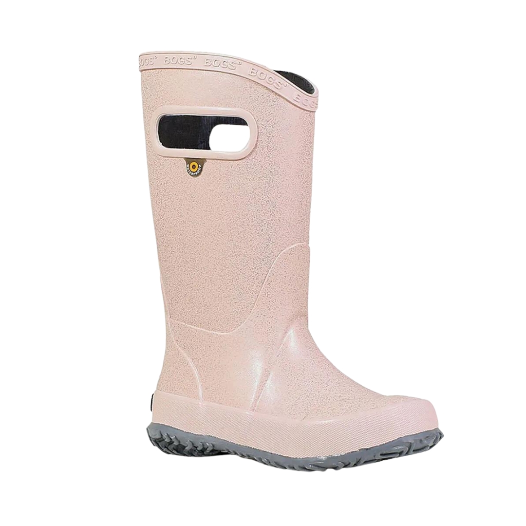 BOTTE DE PLUIE BOGS RAINBOOT GLITTER POUR ENFANT ET JUNIOR couleur rose gold vu de la botte droite de profil avant droit, botte rose pale avec des brillants semelle d'usure grise pale les poignées au haut de la tige sont visibles ainsi que le logo WaterProof servant à accrocher les bottes visible également sous le trou de la poignée le nom bogs est embossé le long du haut de la tige en bordure
