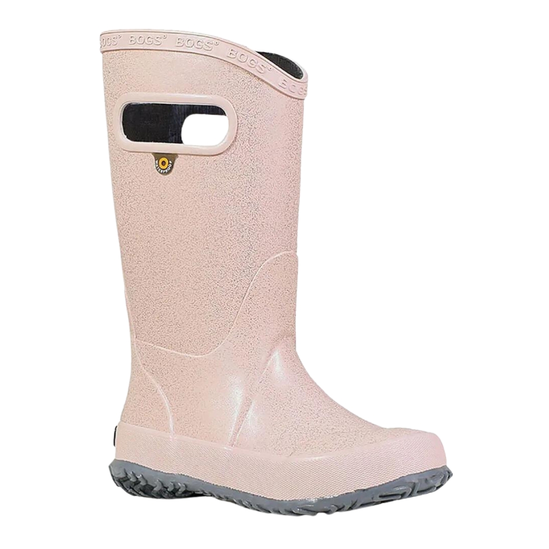 BOTTE DE PLUIE BOGS RAINBOOT GLITTER POUR ENFANT ET JUNIOR couleur rose gold vu de la botte droite de profil avant droit, botte rose pale avec des brillants semelle d'usure grise pale les poignées au haut de la tige sont visibles ainsi que le logo WaterProof servant à accrocher les bottes visible également sous le trou de la poignée le nom bogs est embossé le long du haut de la tige en bordure