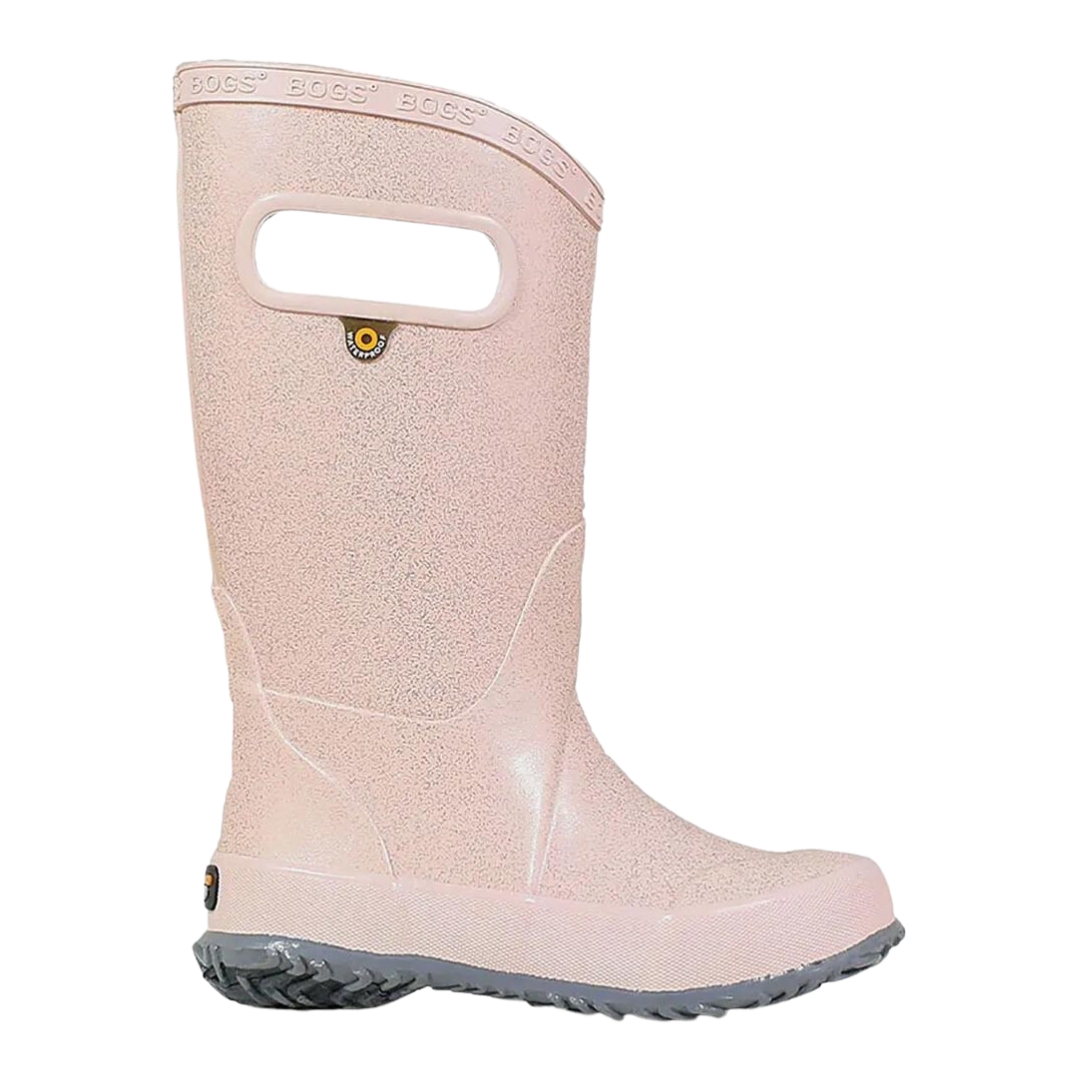 BOTTE DE PLUIE BOGS RAINBOOT GLITTER POUR ENFANT ET JUNIOR couleur rose gold vu de la botte droite de profil droit, botte rose pale avec des brillants semelle d'usure grise pale les poignées au haut de la tige sont visibles ainsi que le logo WaterProof servant à accrocher les bottes visible également sous le trou de la poignée, le nom bogs est embossé le long du haut de la tige en bordure