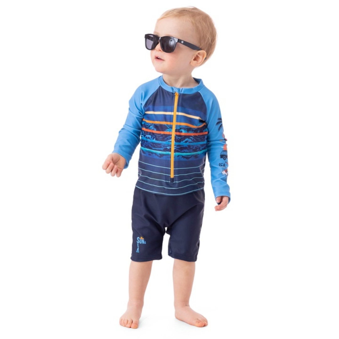 MAILLOT DERMOPROTECTEUR UNE-PIÈCE NANÖ POUR GARÇON COULEUR BLEU PALE VU DU MAILLOT BLEU PALE , MARINE À RAYURES JAUNES ET ORANGE PORTÉ PAR UN GARÇONET