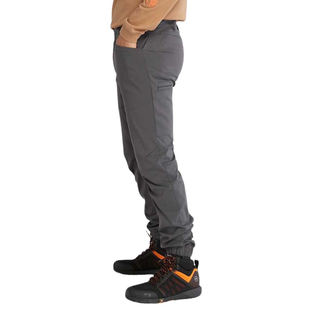 PANTALON JOGGER DE TRAVAIL TIMBERLAND PRO TEMPE POUR HOMME couleur asphalt vu du pantalon long gris foncé porté par un homme vu de la taille aux pieds de profil gauche la main dans la poche latérale