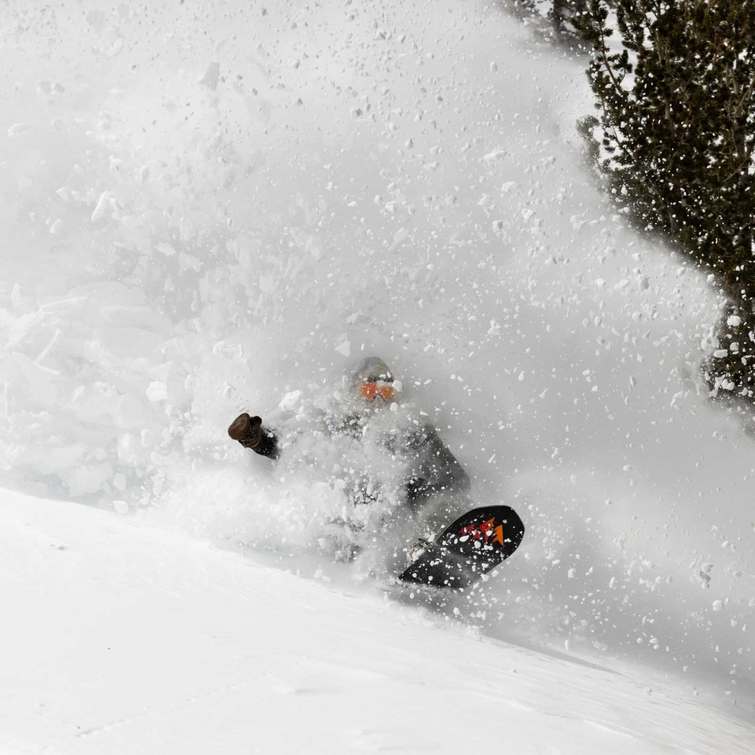PLANCHE À NEIGE JONES STRATOS POUR HOMME vu de la planche rouge et noire utilisée par un homme qui glisse dans la poudreuse