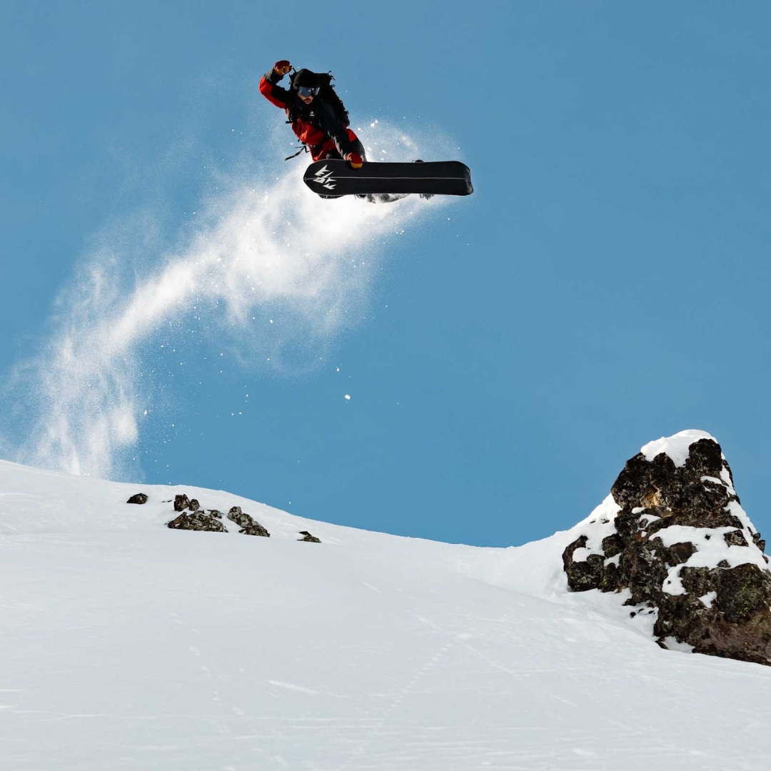 SPLITBOARD JONES STRATOS POUR HOMME vu de la planche blanche lignée rouge et noire utilisé par un homme qui fait un saut