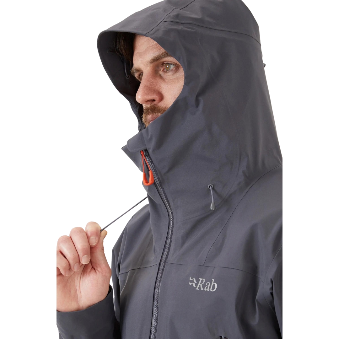 COQUILLE RAB KANGRI GORE-TEX POUR HOMME couleur graphene vu du manteau gris fonbcé et détails orange porté par un homme vu en gros plan du capuchon et de son cordon de serrage avant