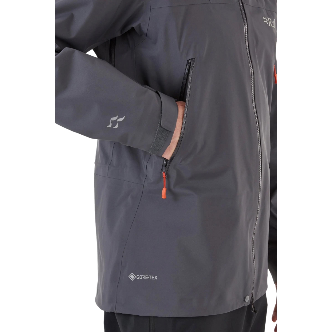 COQUILLE RAB KANGRI GORE-TEX POUR HOMME couleur graphene vu du manteau gris fonbcé et détails orange porté par un homme vu en gros plan sur la poche latérale