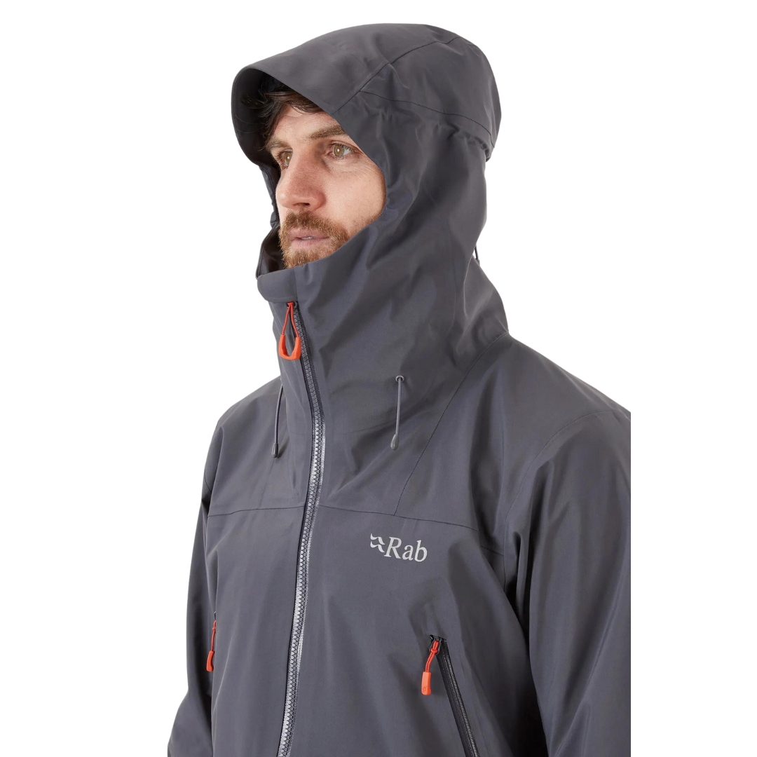 COQUILLE RAB KANGRI GORE-TEX POUR HOMME couleur graphene vu du manteau gris fonbcé et détails orange porté par un homme vu en gros plan sur le haut du manteau l'homme a le capuchon sur la tete