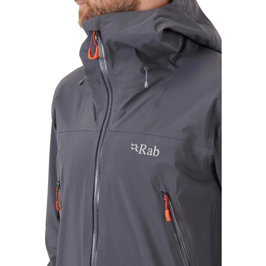 COQUILLE RAB KANGRI GORE-TEX POUR HOMME couleur graphene vu du manteau gris fonbcé et détails orange porté par un homme vu en gros plan sur le nom rab à la poitrine gauche