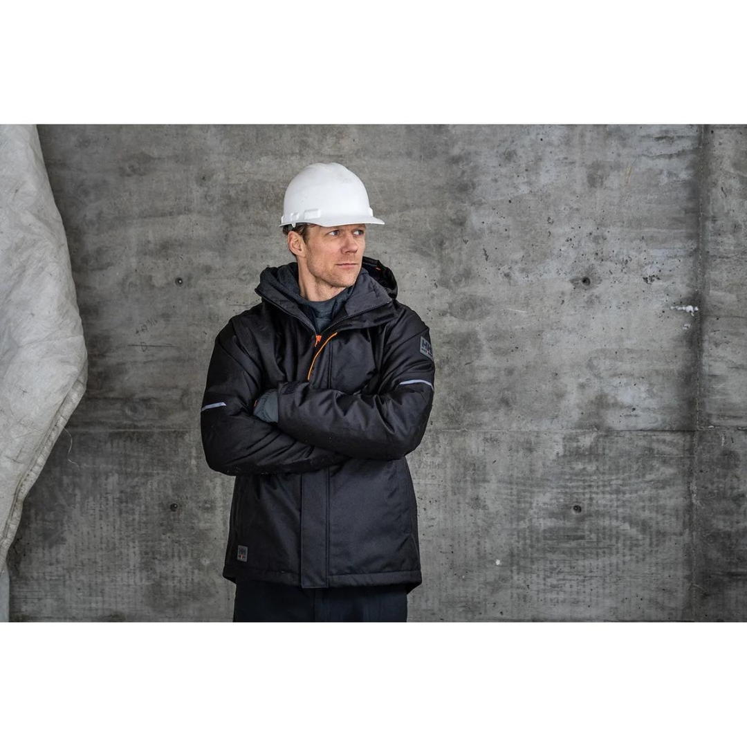 MANTEAU DE TRAVAIL ISOLÉ HELLY HANSEN WORKWEAR KENSINGTON POUR HOMME couleur black vu du manteau noir avec détails orange fluo porté par un homme vu de face les bras croisés