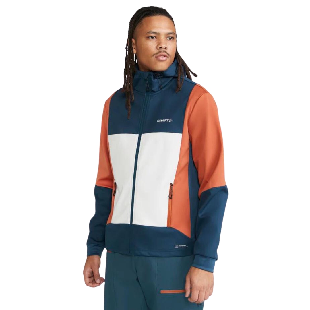 MANTEAU À CAPUCHON DE SKI DE FOND CRAFT CORE BACKCOUNTRY POUR HOMME couleur pond/buff vu du manteau bleu turquoise, orange corail et blanc cassé porté par un homme vu de la tête aux cuisses de profil avant gauche