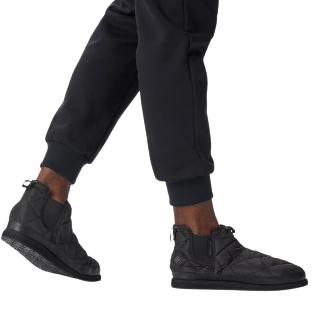 PANTOUFLE COLUMBIA OMNI-HEAT LAZY BEND WEEKENDER COULEUR 010-BLACK/GRAPHITE VU DE LA PANTOUFLE NOIRE PORTÉE PAR UN HOMME VU DES GENOUX AU PIEDS
