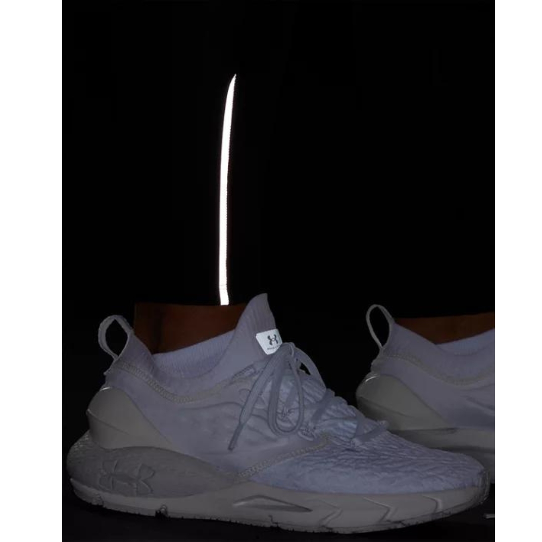 LEGGING LONG UNDER ARMOUR UA FLY FAST 3.0 POUR FEMME couleur 001-BLACK/BLACK/REFLECTIVE vu du leggin noir porté par une femme dans la pénombre vue en gros plan sur le détail réfléchissant à la cheville