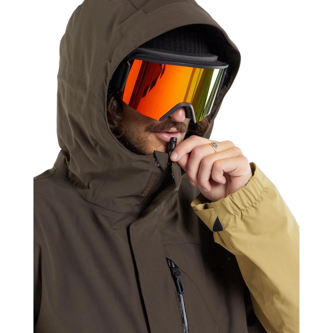 MANTEAU DE SKI EN GORETEX VOLCOM L POUR HOMME couleur brn-brown vu du manteau brun, noir et beige porté par un homme qui utilise la tirette sifflet