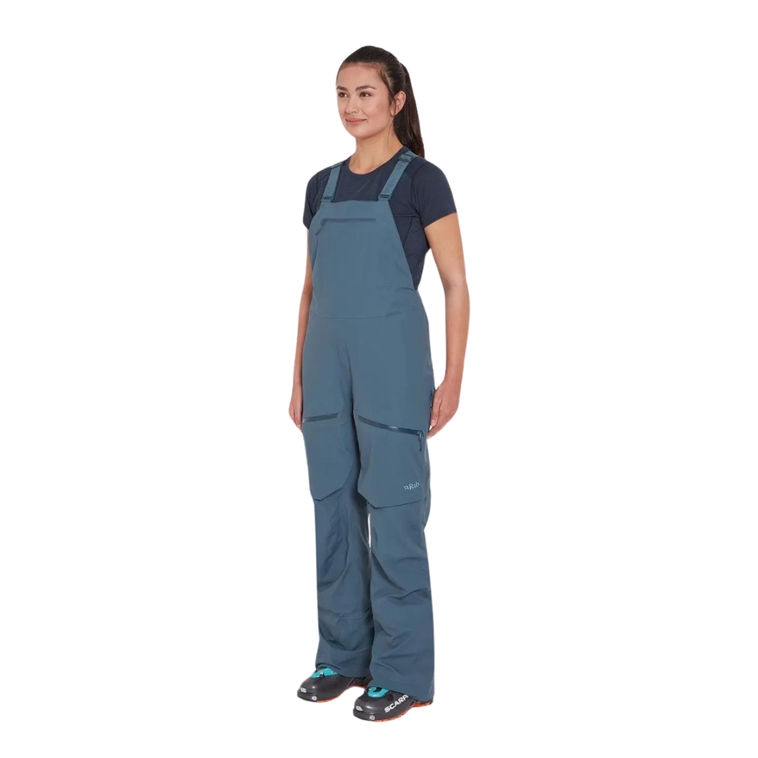 SALOPETTE IMPERMÉABLE DE SKI RAB KHROMA KINETIC POUR FEMME couleur orion blue vue de la salopette bleue acier portée par une femme vue