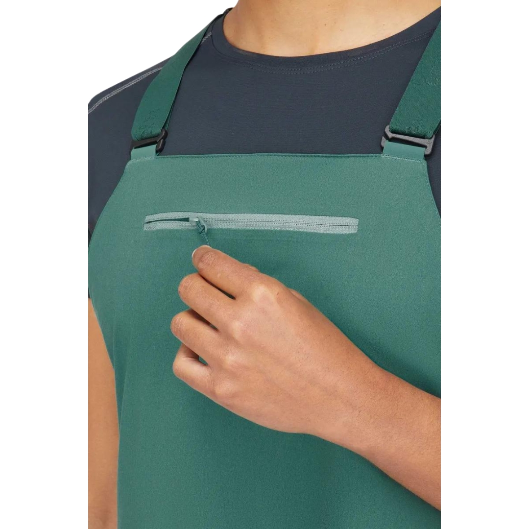 SALOPETTE IMPERMÉABLE DE SKI RAB KHROMA KINETIC POUR FEMME couleur green slate portée par une femme vue ouvran tla poche à fermeture éclair au haut avant