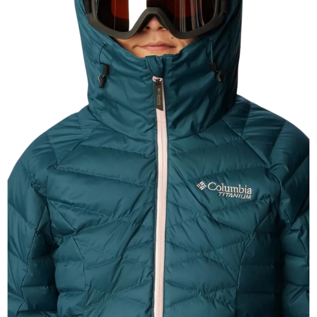 MANTEAU DE SKI ALPIN ISOLÉ EN DUVET COLUMBIA DROARING FORK POUR FEMME couleur 414-NIGHT WAVE vu du manteau turquoise foncé avec fermeture éclair rose pale porté par une femme vue en gros plan sur le col montant et elle porte la capuche