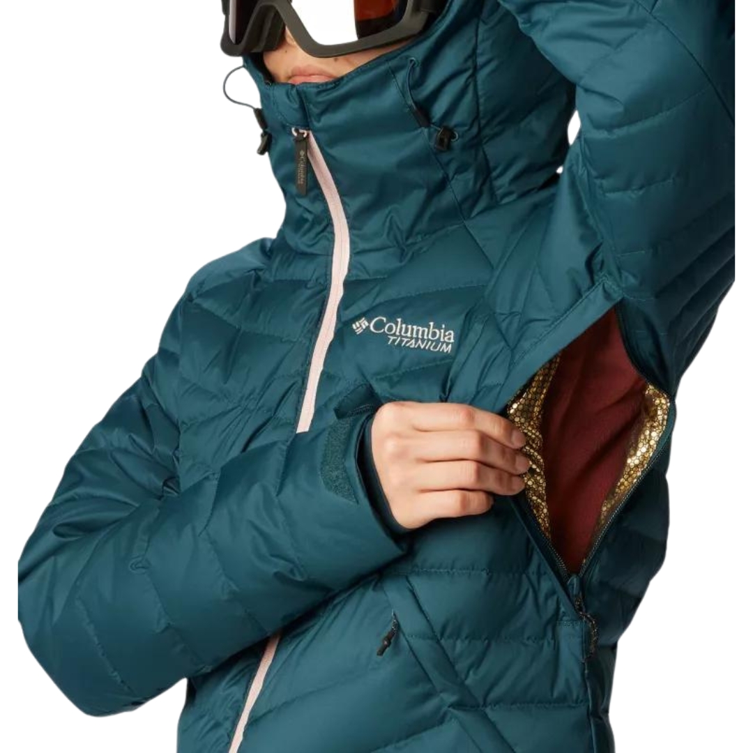 MANTEAU DE SKI ALPIN ISOLÉ EN DUVET COLUMBIA DROARING FORK POUR FEMME couleur 414-NIGHT WAVE vu du manteau turquoise foncé avec fermeture éclair rose pale porté par une femme vue en gros plan sur les fentes sous l'aisselle