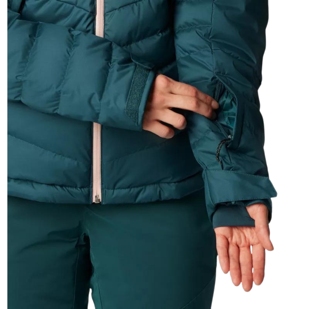 MANTEAU DE SKI ALPIN ISOLÉ EN DUVET COLUMBIA DROARING FORK POUR FEMME couleur 414-NIGHT WAVE vu du manteau turquoise foncé avec fermeture éclair rose pale porté par une femme vue de profil en gros plans sur la poche de manche pour la passe de ski