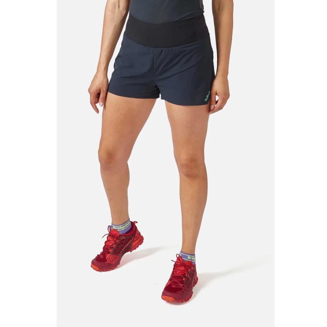 SHORT D'ENTRAINEMENT RAB TALUS TRAIL LIGHT 5'' POUR FEMME couleur ebony porté par une femme vue de l'avant avec le short gris foncé qui tombe au haut de la cuisse avec une bande de taille élastique en noir
