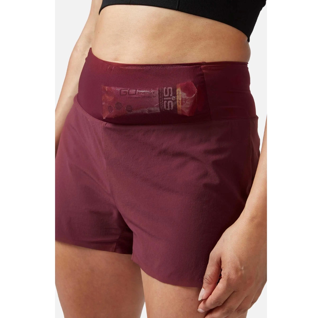 SHORT D'ENTRAINEMENT RAB TALUS TRAIL LIGHT 5'' POUR FEMME porté par une femme qui montre une barre énergétique dans la poche en filet de la taille à l'avant