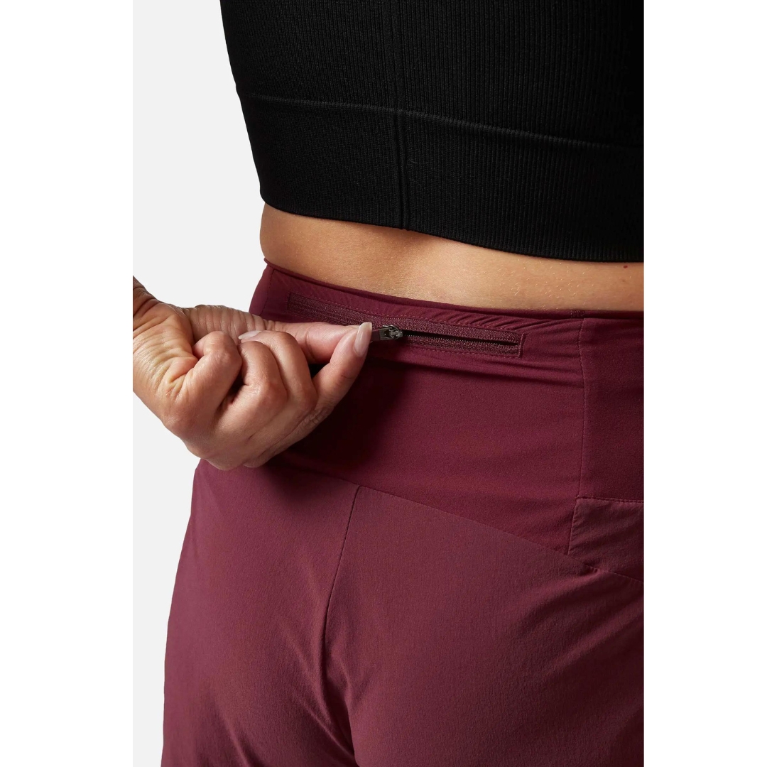 SHORT D'ENTRAINEMENT RAB TALUS TRAIL LIGHT 5'' POUR FEMME porté par une femme qui ouvre la fermeture éclair de la poche de taille arrière