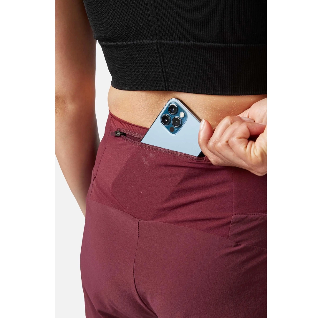SHORT D'ENTRAINEMENT RAB TALUS TRAIL LIGHT 5'' POUR FEMME porté par une femme qui range un téléphone dans la poche arrière à fermeture à glissière