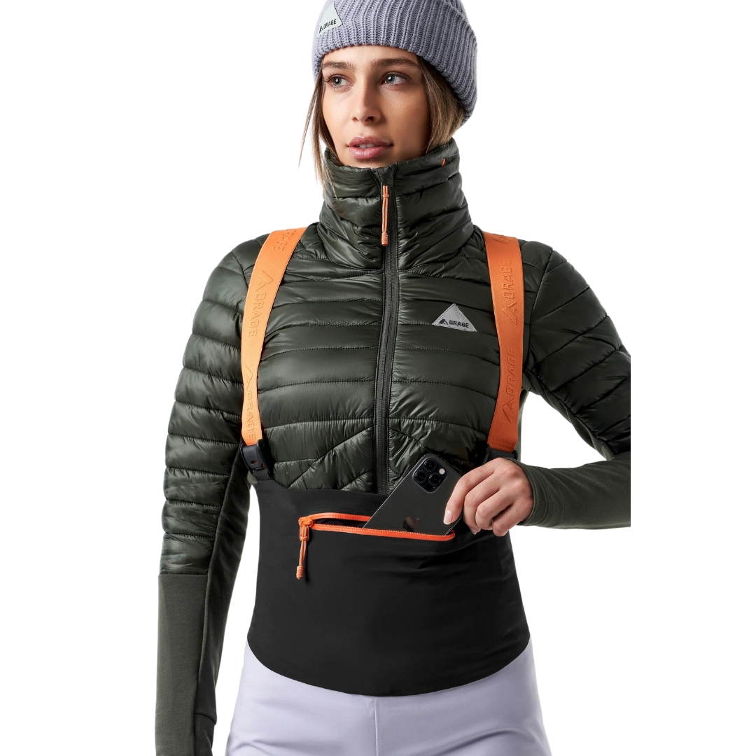 SALOPETTE COQUILLE DE SKI ALPIN ORAGE MTN-X CLIFF POUR FEMME porté par une femme qui montre la poche à fermeture éclair à l'avant de la salopette