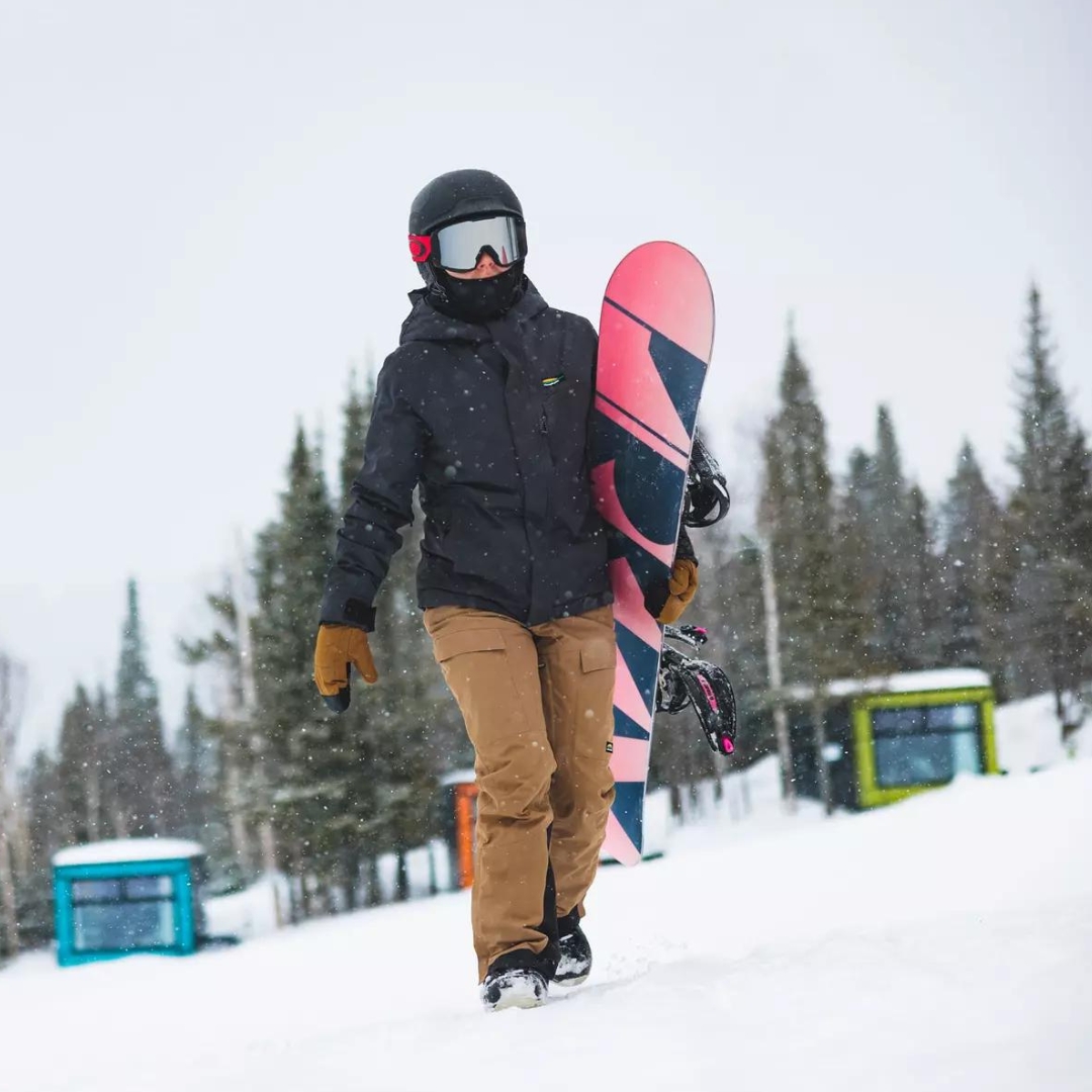 MITAINE DE SKI ALPIN CHLOROPHYLLE GLISSE POUR FEMME COULEUR TABAC VU DE LA MITAINE BRUNE SABLE LETTRÉE BLANCHE PORTÉE PAR UNE FEMME QUI MARCHE AVEC SA PLANCHE À NEIGE