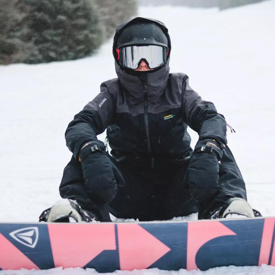 MITAINE DE SKI ALPIN CHLOROPHYLLE GLISSE POUR FEMME COULEUR NOIR PUR VU DE LA MITAINE NOIRE LETTRÉE BLANCHE PORTÉE PAR UNE FEMME QUI EST ASSISE AVEC SA PLANCHE À NEIGE