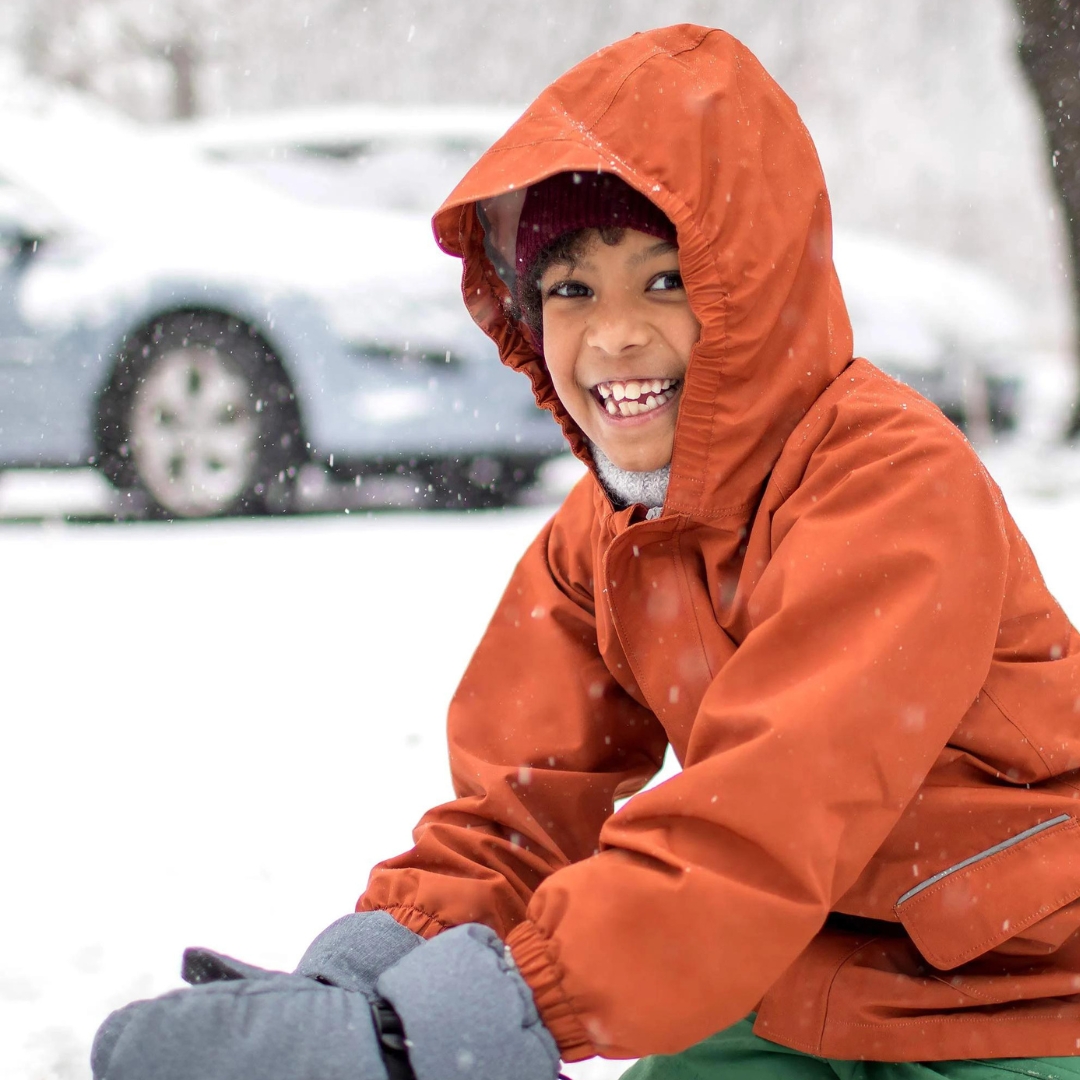 MANTEAU DE PLUIE JAN & JUL PUDDLE-DRY POUR ENFANT couleur TERRACOTTA vu du manteau orange brûlé porté par un enfant dehors dans la neige