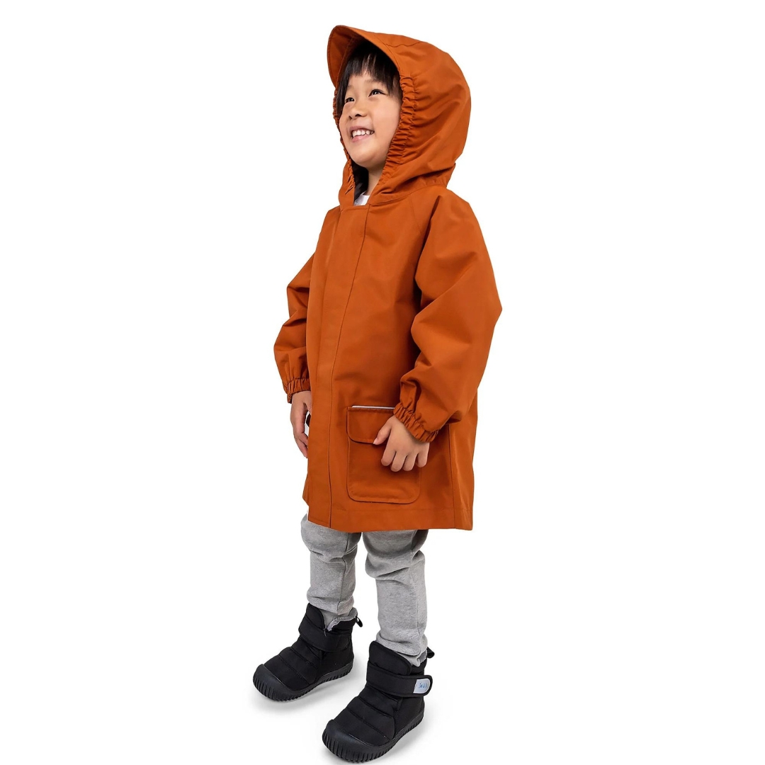 MANTEAU DE PLUIE JAN & JUL PUDDLE-DRY POUR ENFANT couleur TERRACOTTA vu du manteau orange brûlé porté par un enfant vu de la tête aux pieds de profil avant gauche