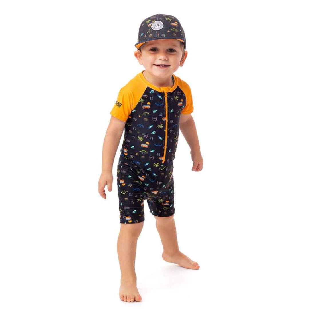 COMBINAISON DE BAIN UV NANÖ À MANCHES COURTES POUR BÉBÉ GARÇON couleur noir vu du maillot noir avec manches jaunes orange et imprimé de dinosore, van, palmier et vagues porté par un garçon vu de la tête aux pieds de face