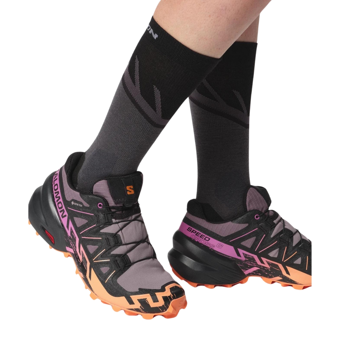 CHAUSSURE DE COURSE SUR SENTIER SALOMON SPEEDCROSS 6 GTX POUR FEMME COULEUR MOONSCAPE/BLACK/BIRD OF PARADISE VU DE LA CHAUSSURE NOIRE, ROSE, MAUVE ET PÊCHE PORTÉES PAR UNE FEMME VUE DES MOLLETS AUX PIEDS DE PROFIL DROIT