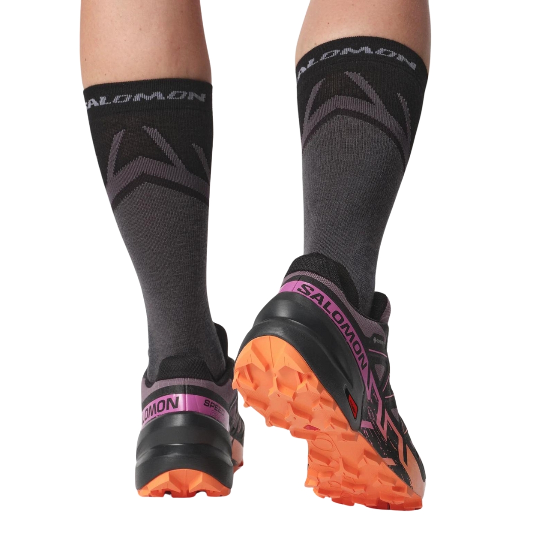 CHAUSSURE DE COURSE SUR SENTIER SALOMON SPEEDCROSS 6 GTX POUR FEMME COULEUR MOONSCAPE/BLACK/BIRD OF PARADISE VU DE LA CHAUSSURE NOIRE, ROSE, MAUVE ET PÊCHE PORTÉES PAR UNE FEMME VUE DES MOLLETS AUX PIEDS DE DOS
