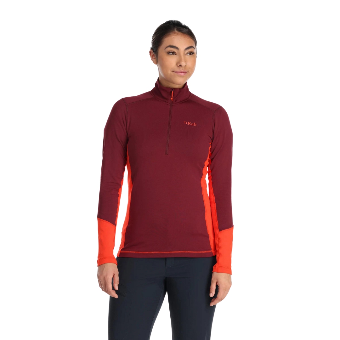 CHANDAIL À MANCHES LONGUES À 1/2 FERMETURE ÉCLAIR RAB CONDUIT POUR FEMME couleur deep heather vu du chandail rouge brique avec détails orange aux manches porté par une femme vue de face de la tête aux cuisses